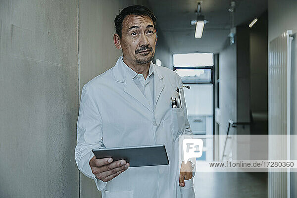 Wissenschaftler mit Hand in der Tasche  der ein digitales Tablet benutzt  während er auf dem Klinikflur steht