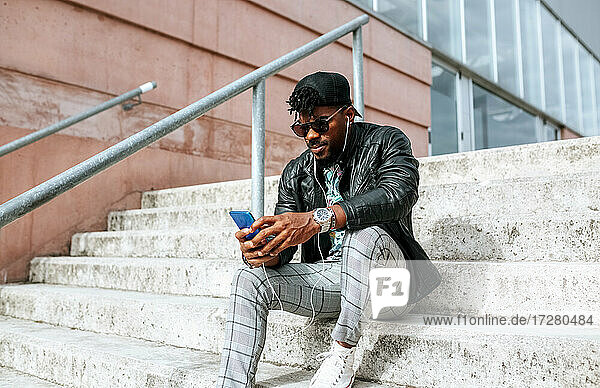 Mid adult man wearing sunglasses using mobile phone while sitting on steps