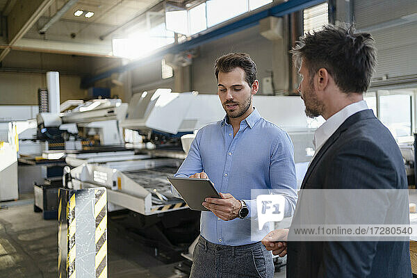 Businessman using digital tablet while standing by colleague at factory