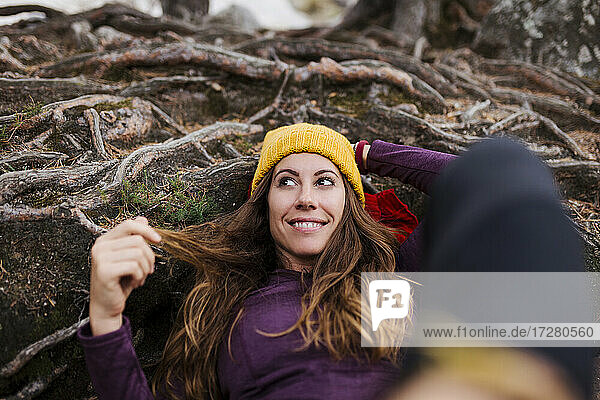 Lächelnde Frau  die wegschaut  während sie auf Baumwurzeln im Wald bei La Pedriza  Madrid  Spanien  liegt