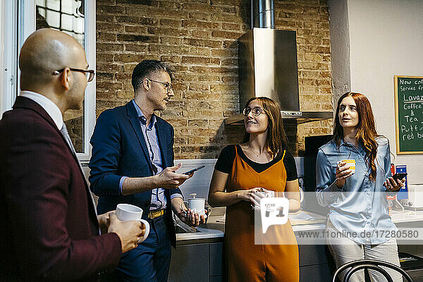 Männliche und weibliche Kollegen diskutieren bei einem Kaffee in der Büroküche