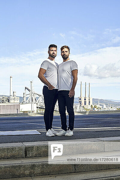 Confident gay couple standing on bridge against sky