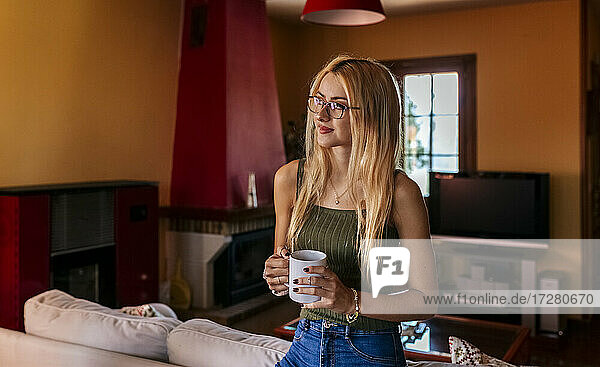 Thoughtful teenage girl holding coffee cup while looking away at home