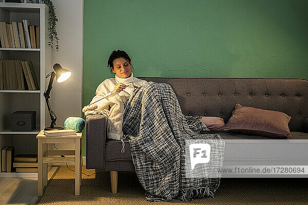 Mittlere erwachsene Frau strickt Wolle  während sie zu Hause auf dem Sofa sitzt