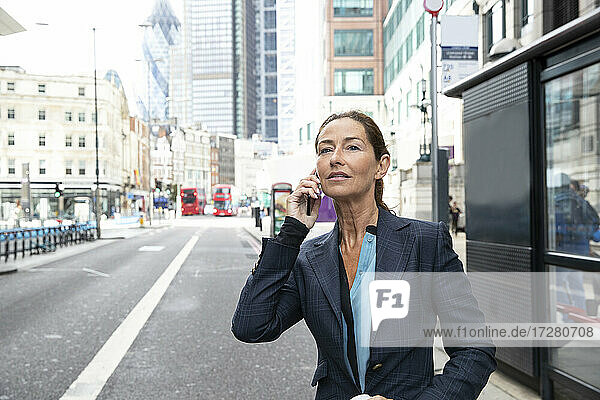Frau in Geschäftskleidung  die auf einer Straße in der Stadt steht und mit einem Mobiltelefon spricht
