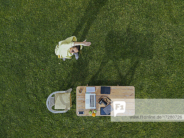 Luftaufnahme einer Frau  die sich vor einem Couchtisch auf grünem Rasen streckt
