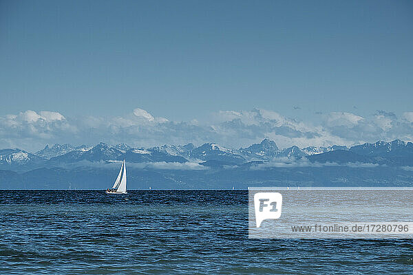 Einsames Segelboot auf dem blauen Wasser des Bodensees mit den Alpen im Hintergrund