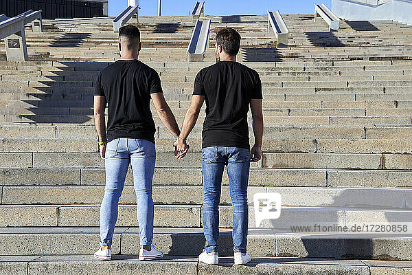 Homosexuelles Paar hält sich an den Händen  während es an einem sonnigen Tag auf einer Treppe steht