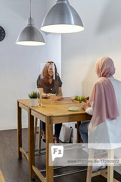 Mitarbeiterin isst Essen  während sie an einem Tisch mit Bildschirmteilung im Büro sitzt