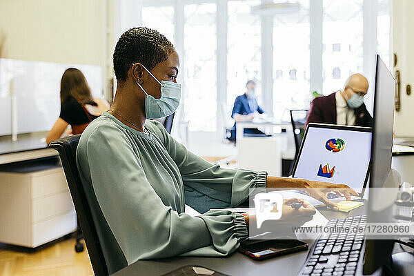Afrikanische Geschäftsfrau mit Schutzmaske bei der Arbeit am Schreibtisch