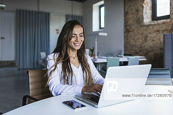 Cheerful businesswoman using laptop at desk in office