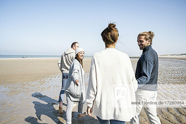 Reifes und junges Paar hält sich beim Strandspaziergang an den Händen
