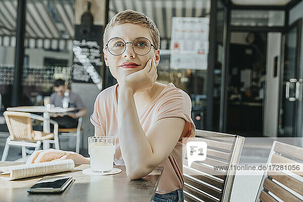 Frau sitzt mit Hand am Kinn in einem Straßencafé an einem sonnigen Tag