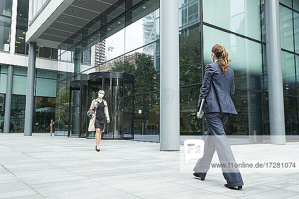 Business people wearing face mask while walking against office building