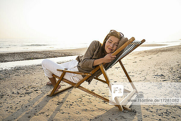 Entspannte Frau  die sich auf einem Klappstuhl am Strand gegen den klaren Himmel bei Sonnenuntergang ausruht