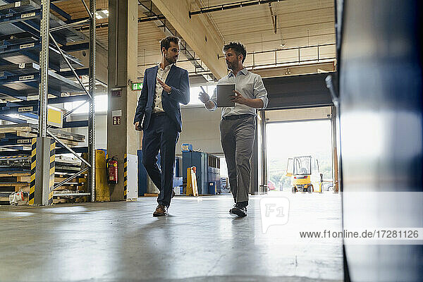 Geschäftsmann und Kollege mit digitalem Tablet im Gespräch beim Spaziergang in einer Fabrik