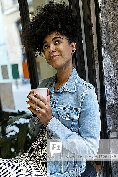 Mittlere erwachsene Frau mit Kaffeetasse  die am Fenster eines Cafés sitzt und nach oben schaut