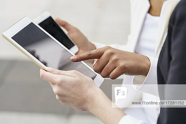 Geschäftsfrau  die auf ein digitales Tablet zeigt  während ein Kollege ein Mobiltelefon hält