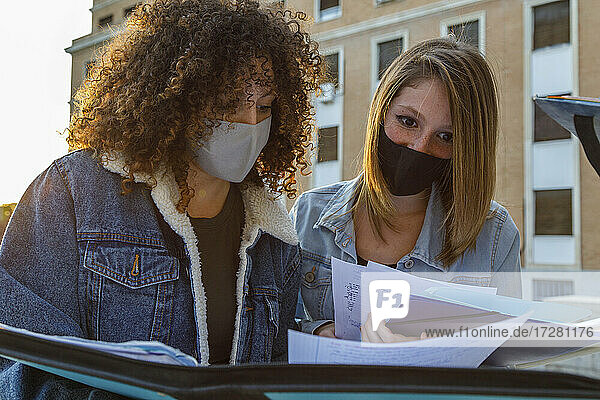 Freundinnen  die mit Schutzmaske studieren  während sie auf dem Universitätscampus vor einem Bildungsgebäude stehen