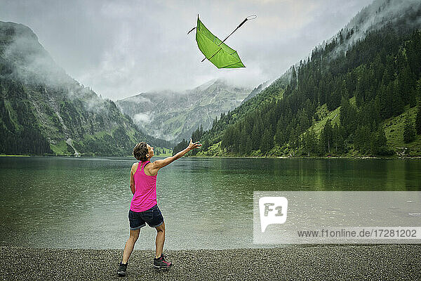 Playful woman catching green umbrella at lakeshore during rainy season