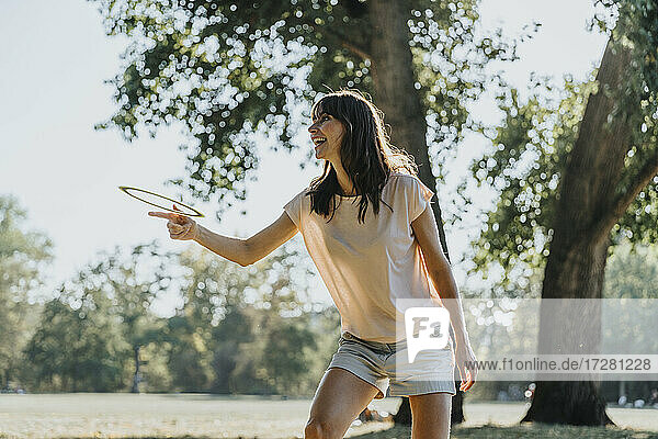 Glückliche reife Frau  die einen Frisbee-Ring wirft  während sie in einem öffentlichen Park an einem sonnigen Tag steht