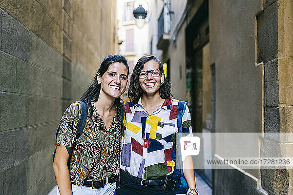 Happy lesbian couple smiling while standing on alley amidst building in city