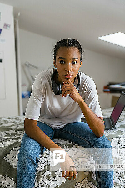 Teenager-Mädchen mit Hand auf dem Kinn sitzt im Schlafzimmer zu Hause