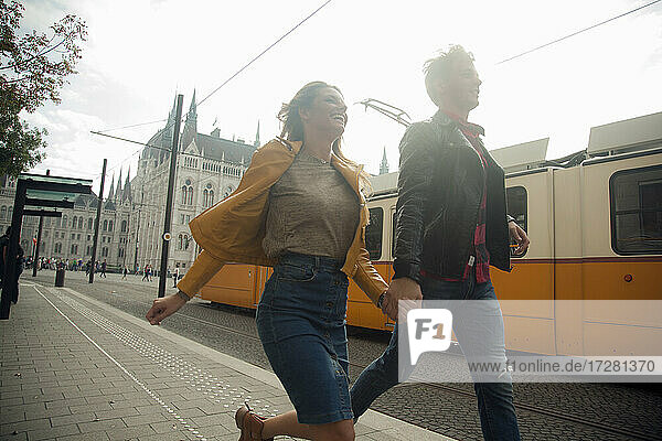 Happy woman holding hands with male partner while running in city