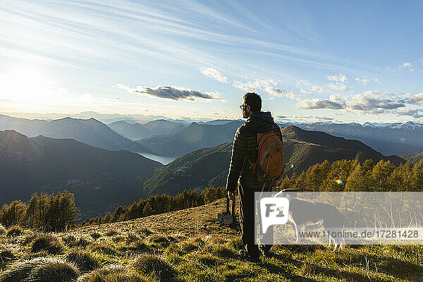 Hiker standing by dog while looking at mountain range during sunset