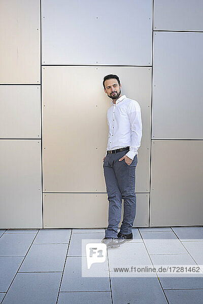 Confident entrepreneur with hands in pockets standing against wall