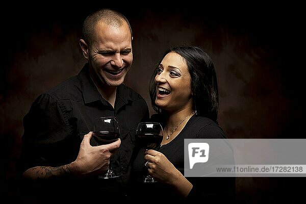 Glückliche junge gemischtrassige Paar hält Weingläser gegen einen schwarzen Hintergrund
