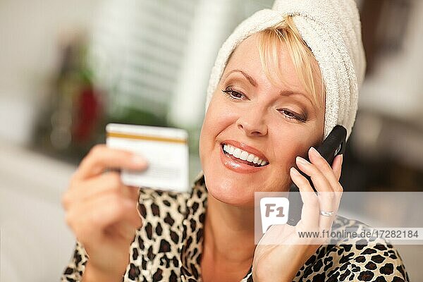 Smiling robed woman on cell phone looking at her credit card