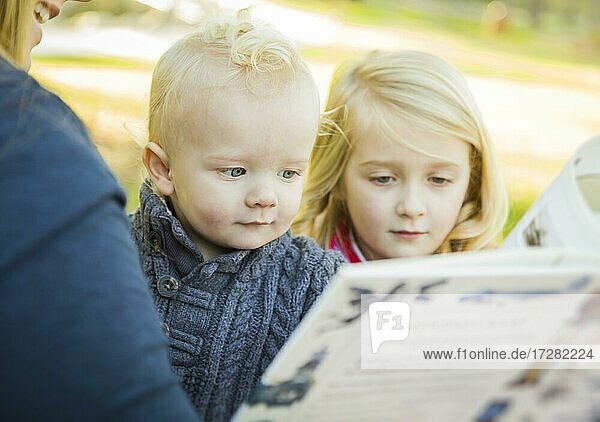 Mutter liest ein Buch zu ihren beiden entzückenden blonden Kinder tragen Wintermäntel im Freien