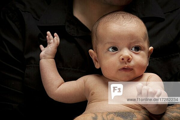 Young father with tattoo holding his mixed-race newborn baby under dramatic lighting