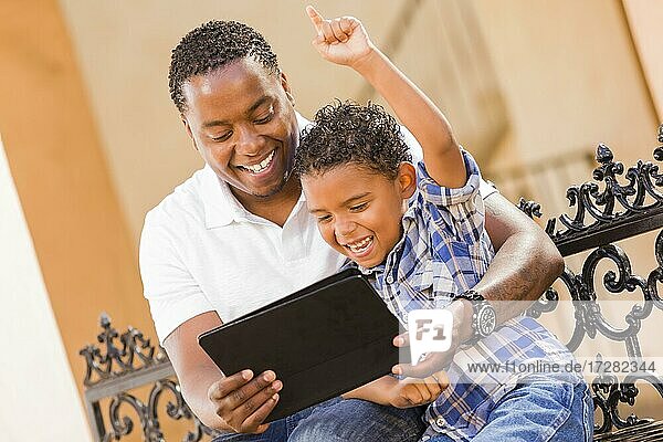 Happy african american father and mixed-race son having fun using touch pad computer tablet outside