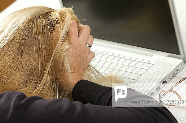 Frau hält ihren Kopf in Frustration  während sie ihren Laptop benutzt
