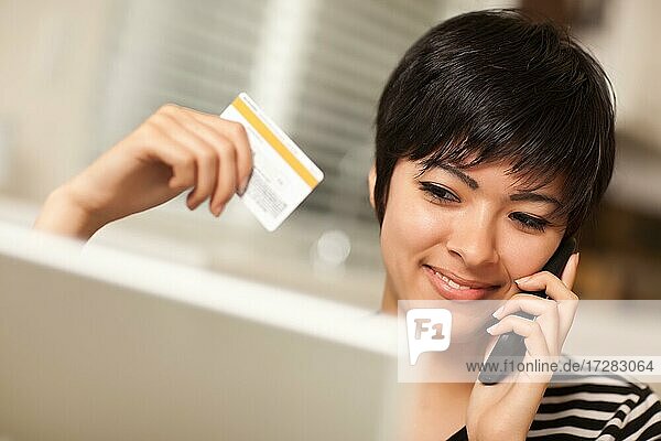 Hübsche junge multiethnische Frau hält Telefon und Kreditkarte mit Laptop
