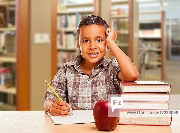 Adorable hispanischen Jungen mit Bücher  Apfel  Bleistift und Papier studieren in der Bibliothek