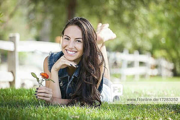 Attractive mixed-race girl portrait laying in grass outdoors with flower