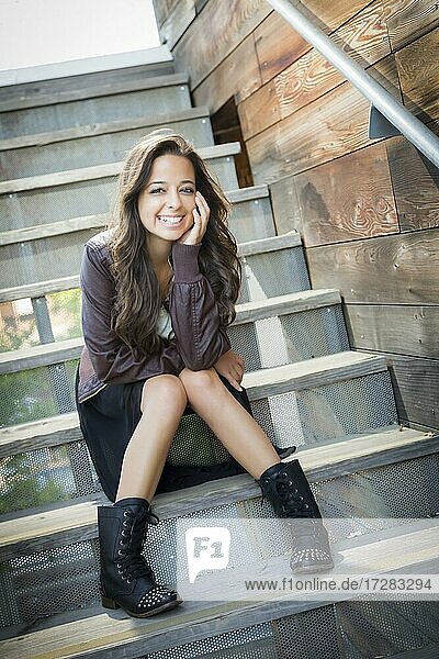 Portrait of a pretty mixed-race young adult woman sitting on a staircase wearing leather boots and jacket