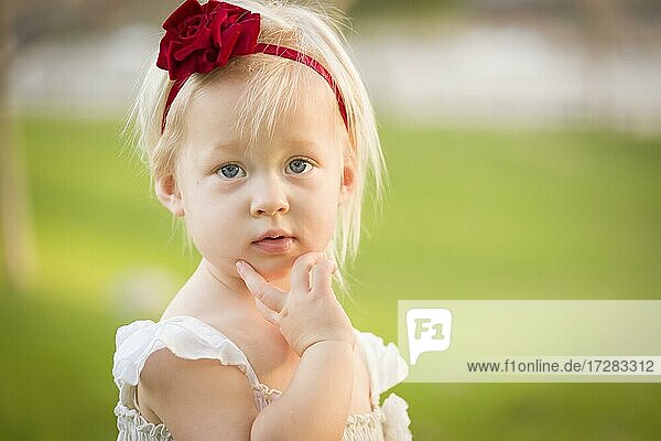 Beautiful adorable little girl with her hand on her face wearing white dress in A grass field