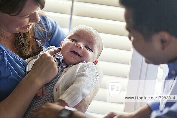 Glückliches gemischtrassiges Paar  das seinen neugeborenen Sohn im Licht des Fensters genießt