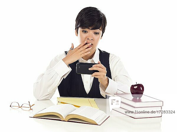 Pretty mixed-race female student at desk with books has shocked look from cell phone message isolated on a white background
