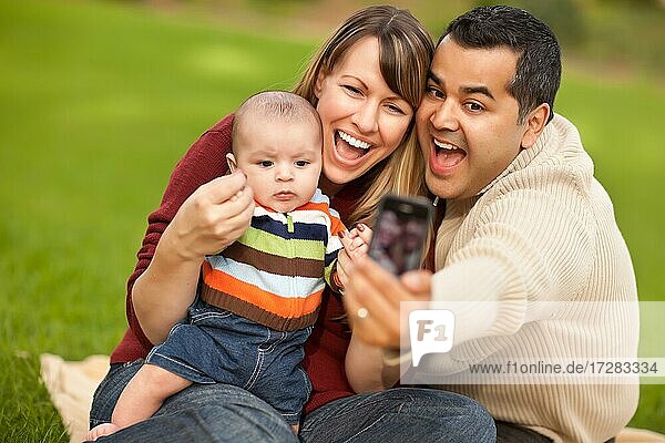 Happy mixed-race parents and baby boy taking self portraits at the park