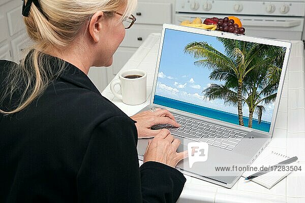 Frau in der Küche mit Laptop zu recherchieren Reisen und Urlaub. Bildschirm kann leicht für Ihre eigene Nachricht oder Bild verwendet werden