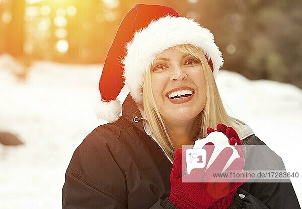 Attractive santa hat wearing blond woman having fun in the snow on a winter day