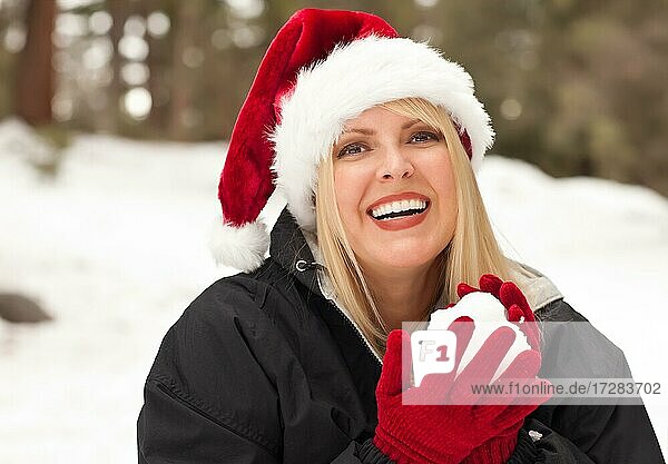Attractive santa hat wearing blond woman having fun in the snow on a winter day