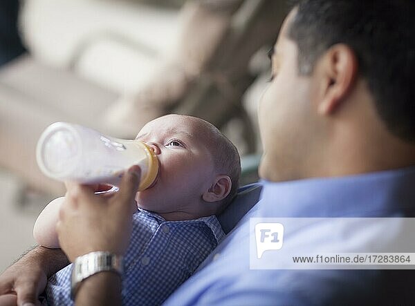 Glücklicher hispanischer Vater füttert seinen sehr zufriedenen gemischtrassigen Sohn mit der Flasche