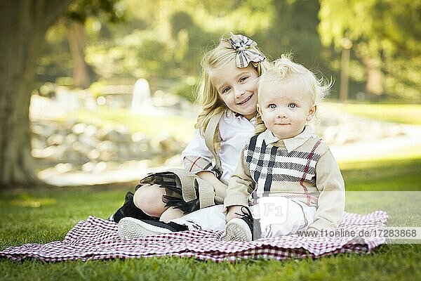 Sweet little girl sitting with her baby brother on a picnic blanket outdoors at the park