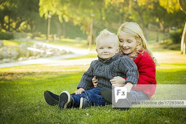 Little girl with her baby brother wearing winter coats outdoors sitting at the park